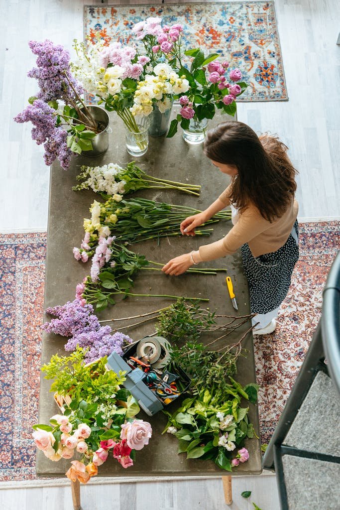 Woman arranging a vibrant flower bouquet on a wooden table in a studio setting.